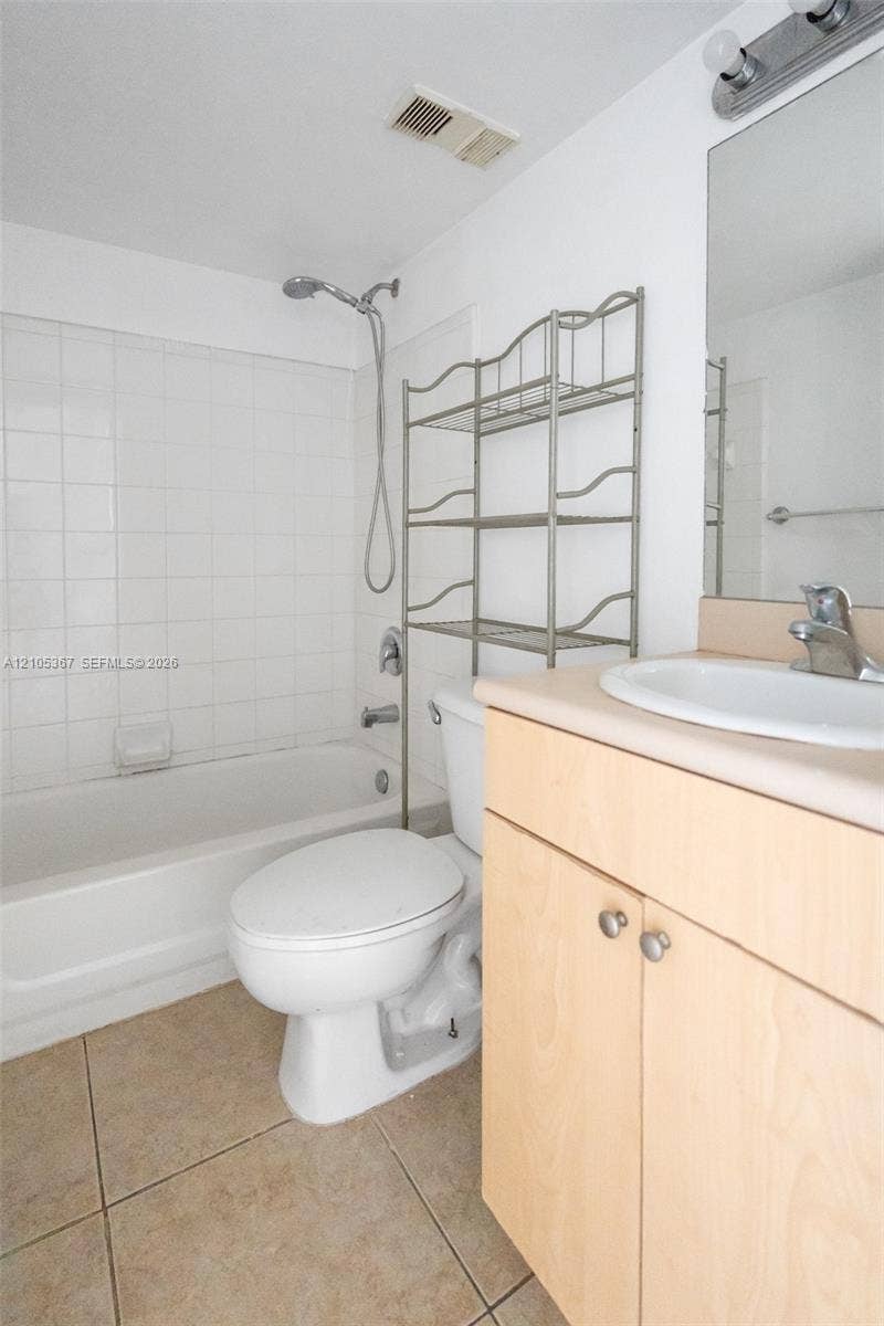 9066 W Atlantic Boulevard, #412, Coral Springs, FL 33071 Bathroom featuring a shower and tub combination with wall-surround tile, vanity with a light-wood finish, solid-surface countertop with an integrated basin, and neutral floor tile