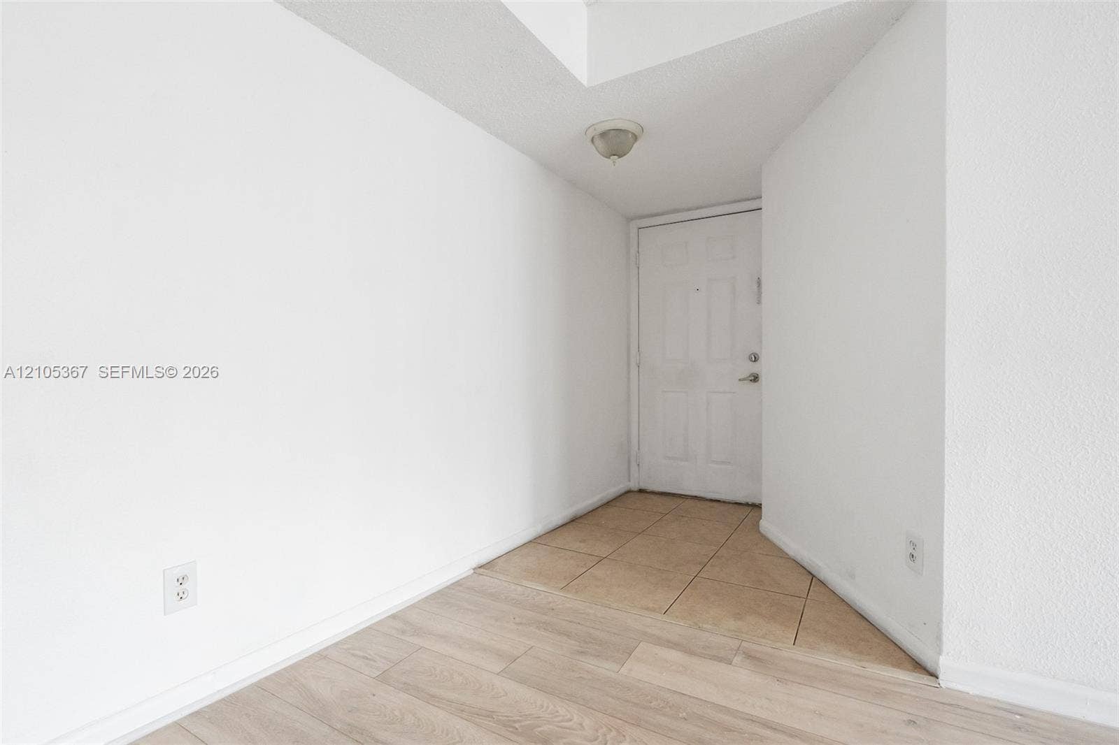 9066 W Atlantic Boulevard, #412, Coral Springs, FL 33071 Entry featuring neutral-toned ceramic tile flooring, wood-finish flooring, a white paneled door, and a flush-mount ceiling light fixture