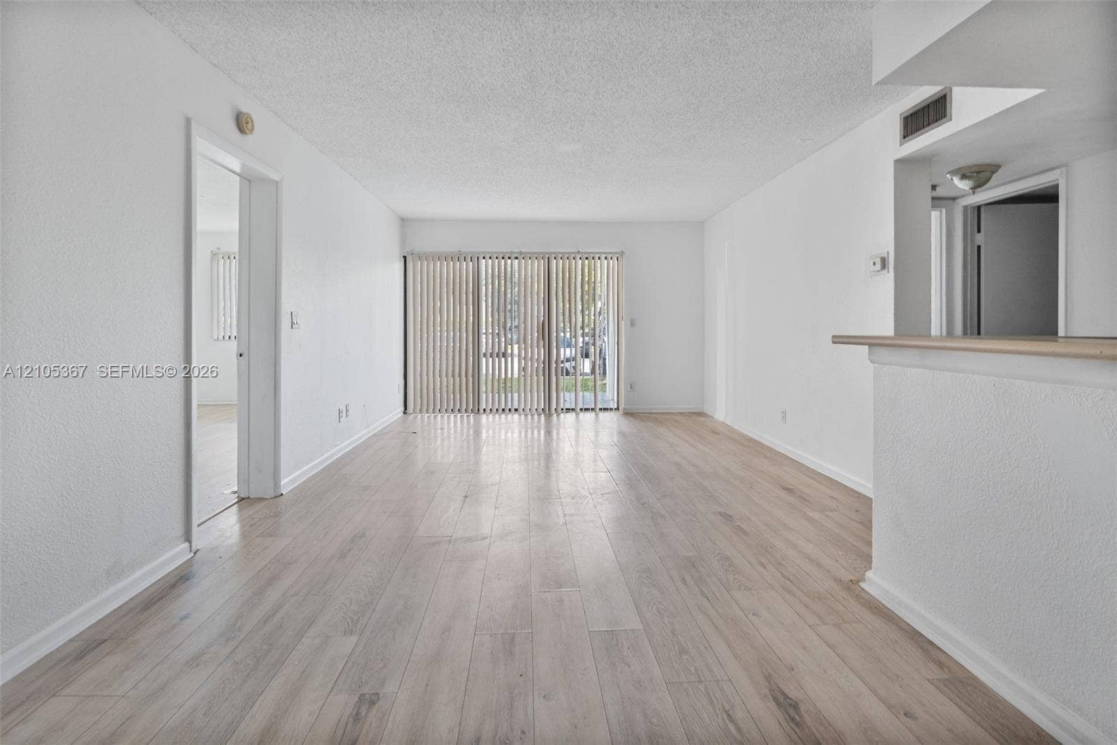 9066 W Atlantic Boulevard, #412, Coral Springs, FL 33071 Interior space featuring wood-finish flooring, textured ceilings, and a sliding glass door with vertical blinds