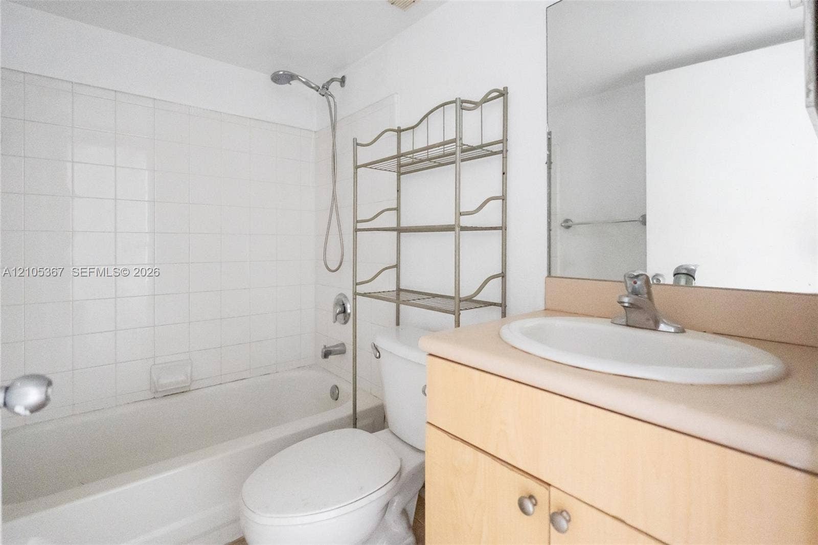 9066 W Atlantic Boulevard, #412, Coral Springs, FL 33071 Bathroom featuring a bathtub with a tiled surround, a showerhead on a flexible hose, a wood-finish vanity with a molded countertop sink, and a wall-mounted mirror