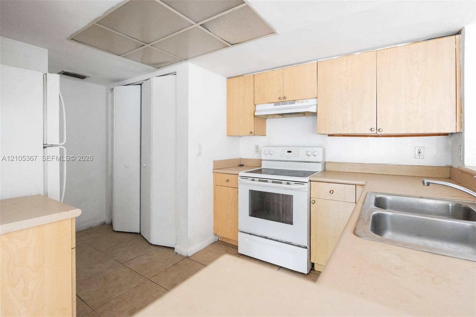 9066 W Atlantic Boulevard, #412, Coral Springs, FL 33071 Kitchen featuring light-finish cabinetry, solid-surface countertops, dual-basin stainless steel sink, integrated range, and ceramic tile flooring