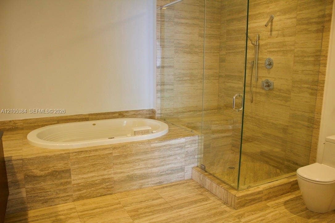 16001 Collins Avenue, #2803, Sunny Isles Beach, Sunny Isles Beach, FL 33160 Recessed soaking tub, glass-enclosed shower with a handheld shower fixture, and a toilet, all set within a natural stone-tiled floor and wall surround