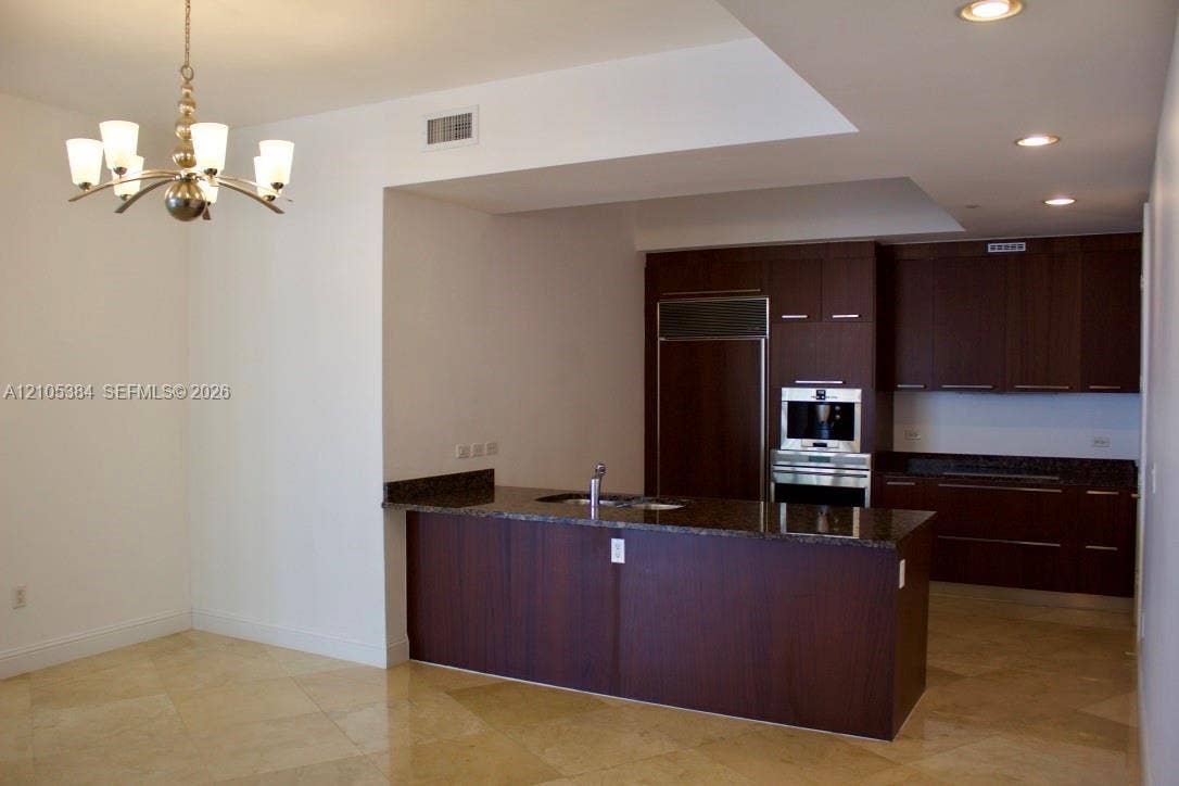 16001 Collins Avenue, #2803, Sunny Isles Beach, Sunny Isles Beach, FL 33160 Kitchen featuring dark wood-finish cabinetry, integrated stainless steel appliances, a center island with a dark countertop, and recessed lighting