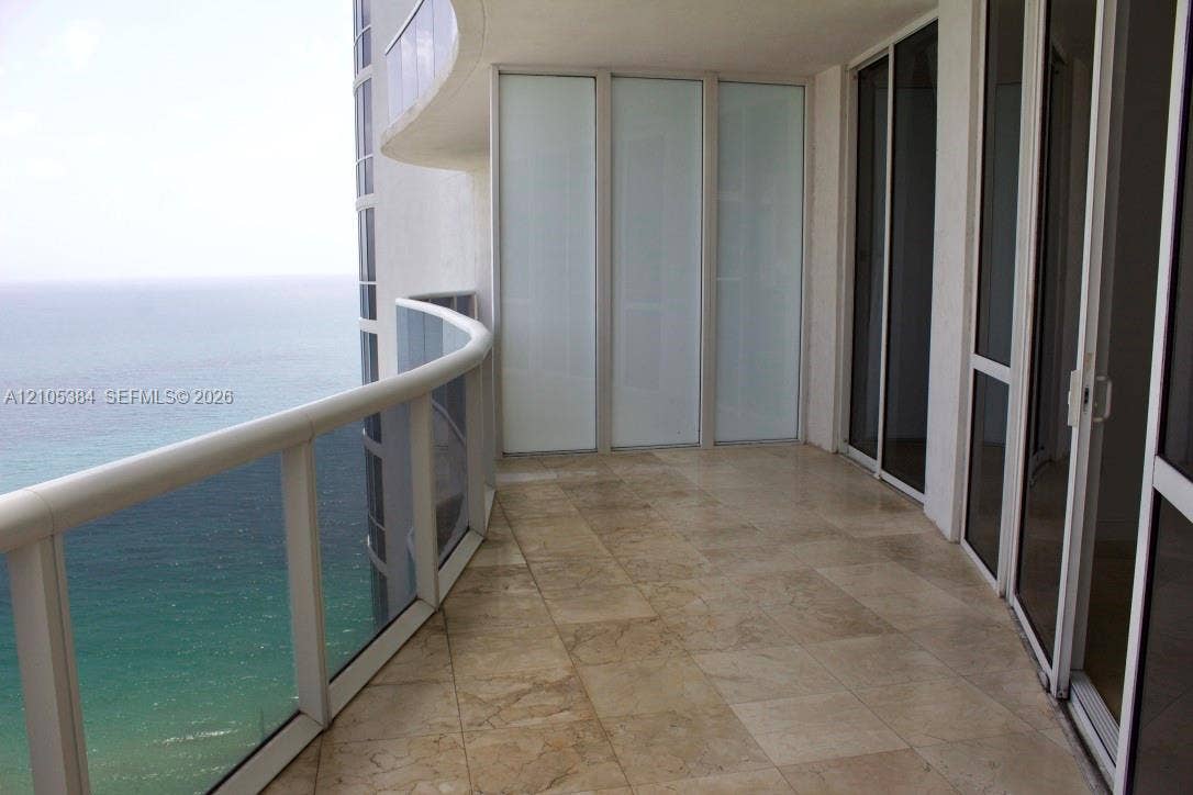 16001 Collins Avenue, #2803, Sunny Isles Beach, Sunny Isles Beach, FL 33160 Curved balcony with glass railing, large format stone-finish tile flooring, and multiple glass sliding doors