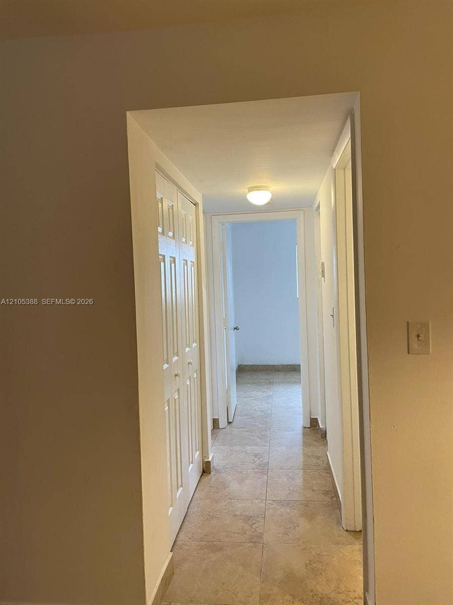 Hallway featuring light-toned tile flooring, flush mount lighting, and white paneled doors