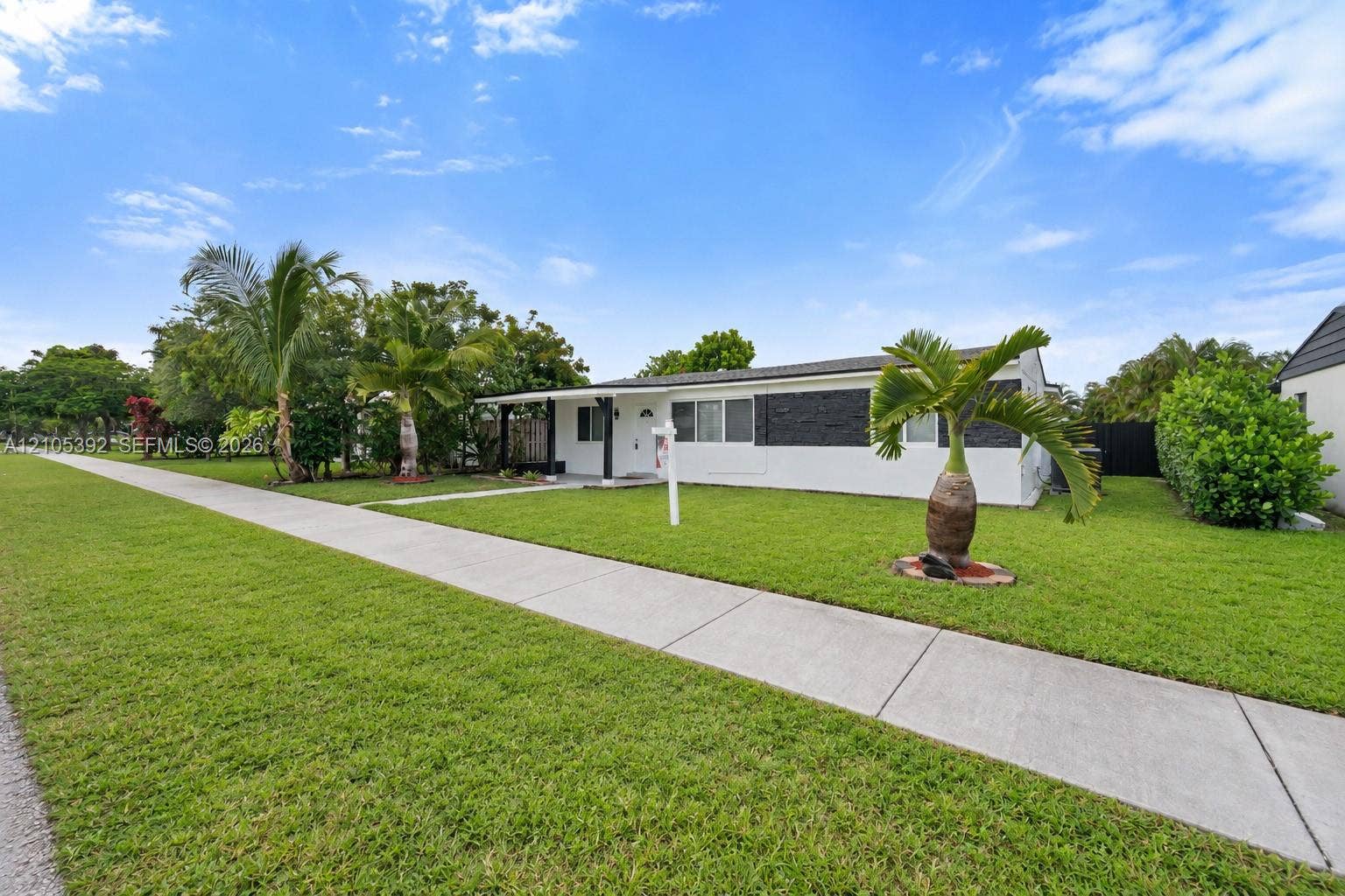 3197 Cleveland Street, Hollywood, FL 33021 White exterior with black accent siding, covered entry, front lawn, and mature palm trees