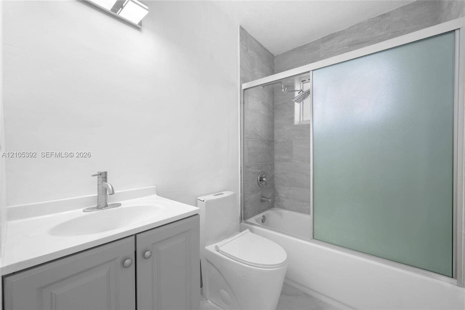 3197 Cleveland Street, Hollywood, FL 33021 Bathroom featuring a vanity with a white countertop and gray cabinetry, a toilet, a tiled shower/tub combination with a sliding frosted glass enclosure, and a chrome faucet