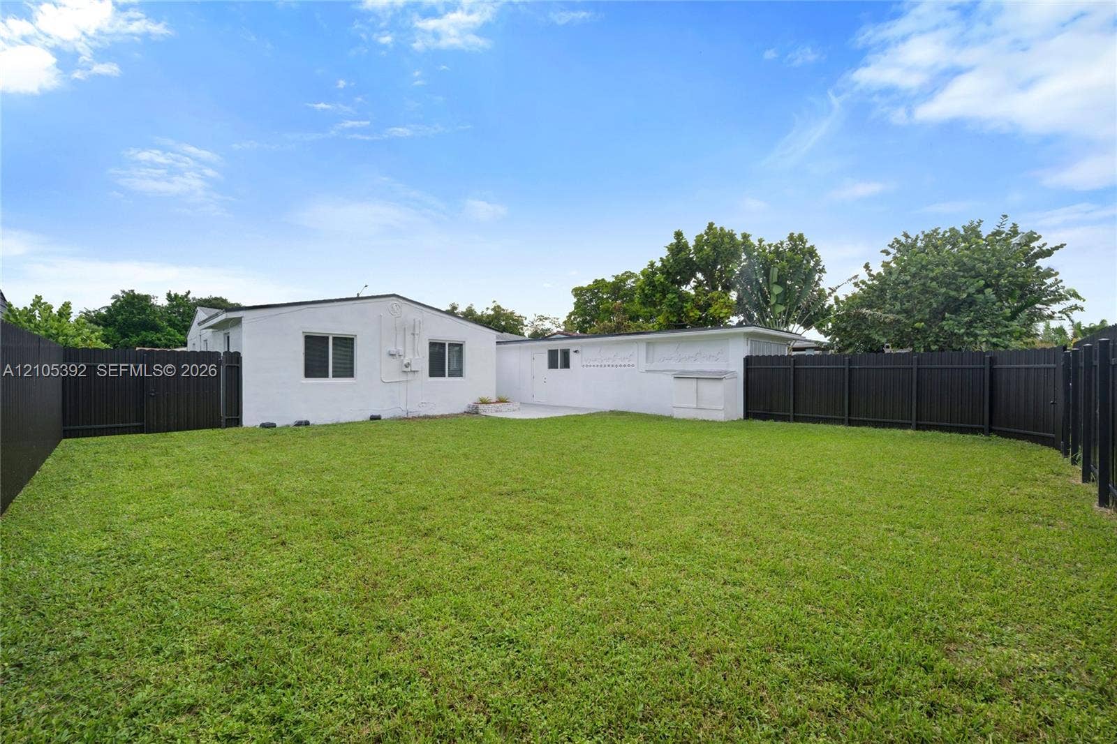 3197 Cleveland Street, Hollywood, FL 33021 Expansive backyard with a manicured lawn, dark fencing, and a white stucco exterior