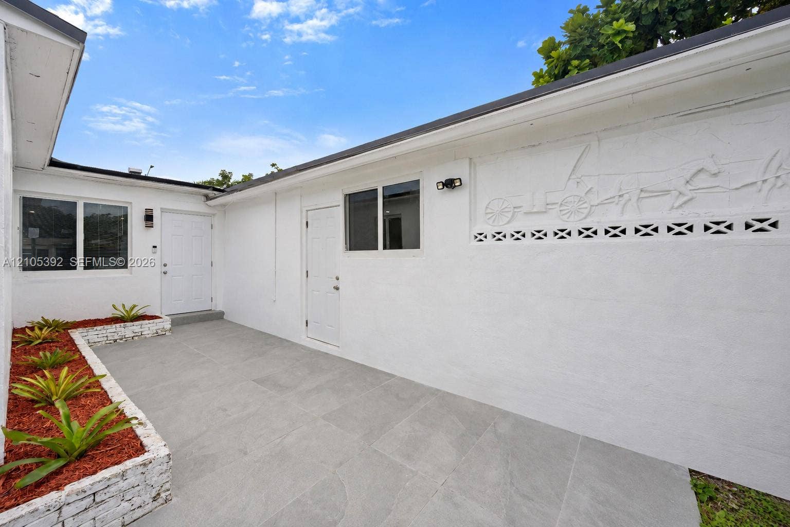3197 Cleveland Street, Hollywood, FL 33021 Exterior patio with large format tile, white stucco walls, windows, and decorative wall relief