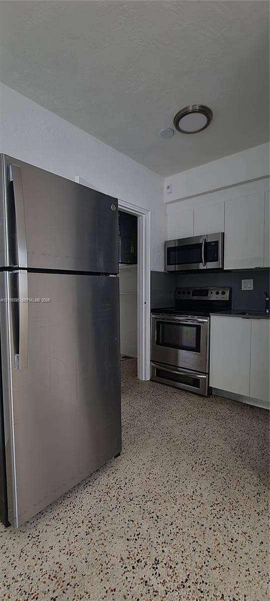 Stainless steel appliance suite, white flat-panel cabinetry, black countertops, and terrazzo flooring