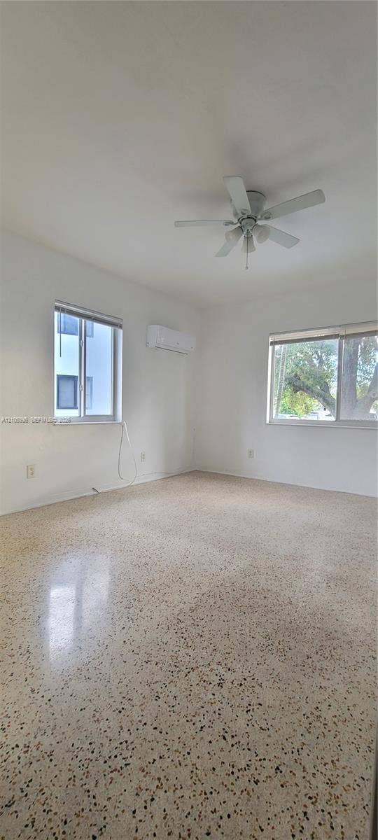 Polished terrazzo flooring, dual windows, ceiling fan, and wall-mounted air conditioning unit