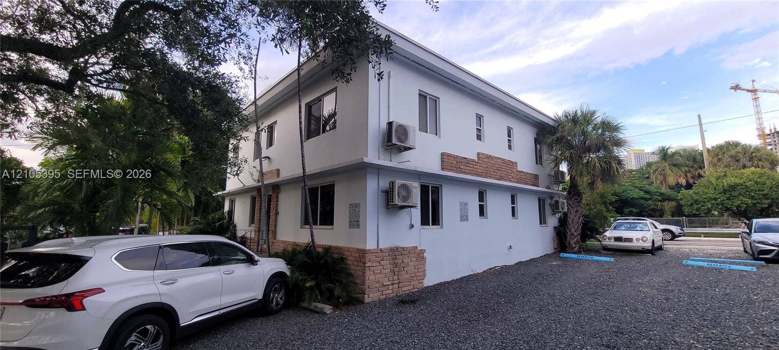 Two-story building featuring a stucco exterior with stone accents, multiple window units, and a gravel parking area
