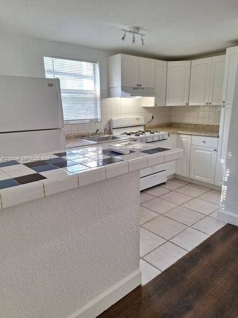 Kitchen featuring white cabinetry, tile countertops, stainless steel sink, and tile flooring