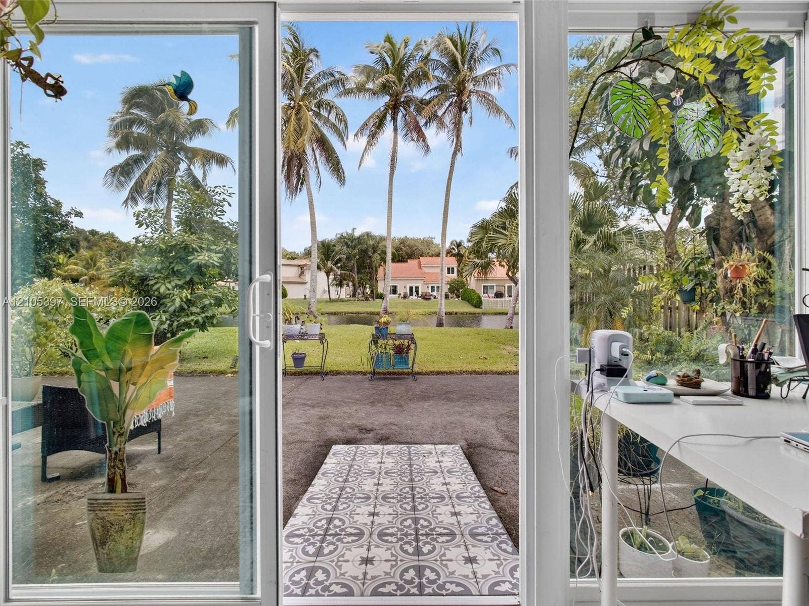 White-framed sliding glass doors opening to a concrete patio, canal-front lot, and mature palm trees