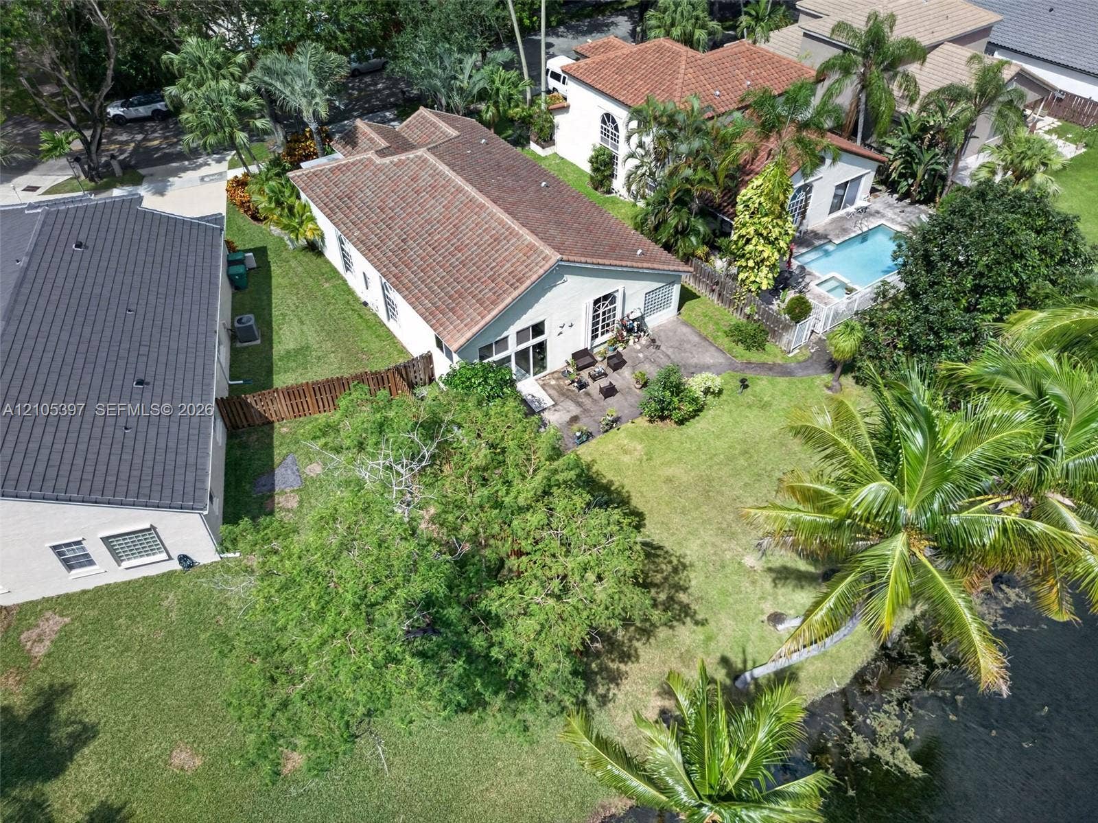 Aerial view of this residence showcasing a sprawling manicured lawn, mature landscaping with native tropical vegetation, and a resort-style pool with surrounding hardscape