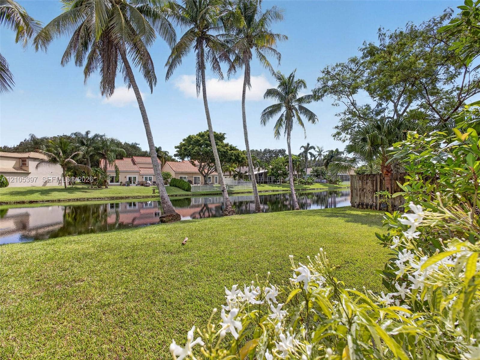 Waterfront lot featuring a manicured lawn, mature palm trees, and a wooden privacy screen. Plenty of room for a pool here!