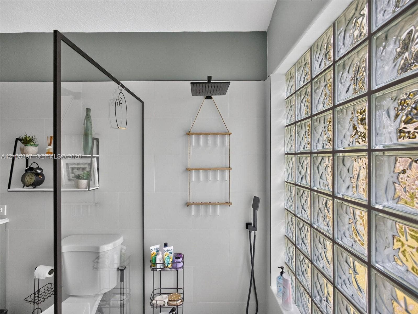 Shower featuring a rainfall showerhead, a separate handheld sprayer, a glass wall panel with a matte black frame.