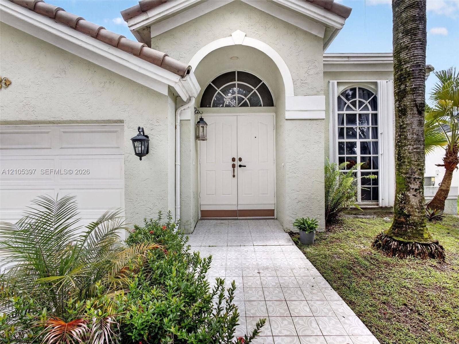 Stucco exterior featuring an arched entryway with a ramp, to double doors.