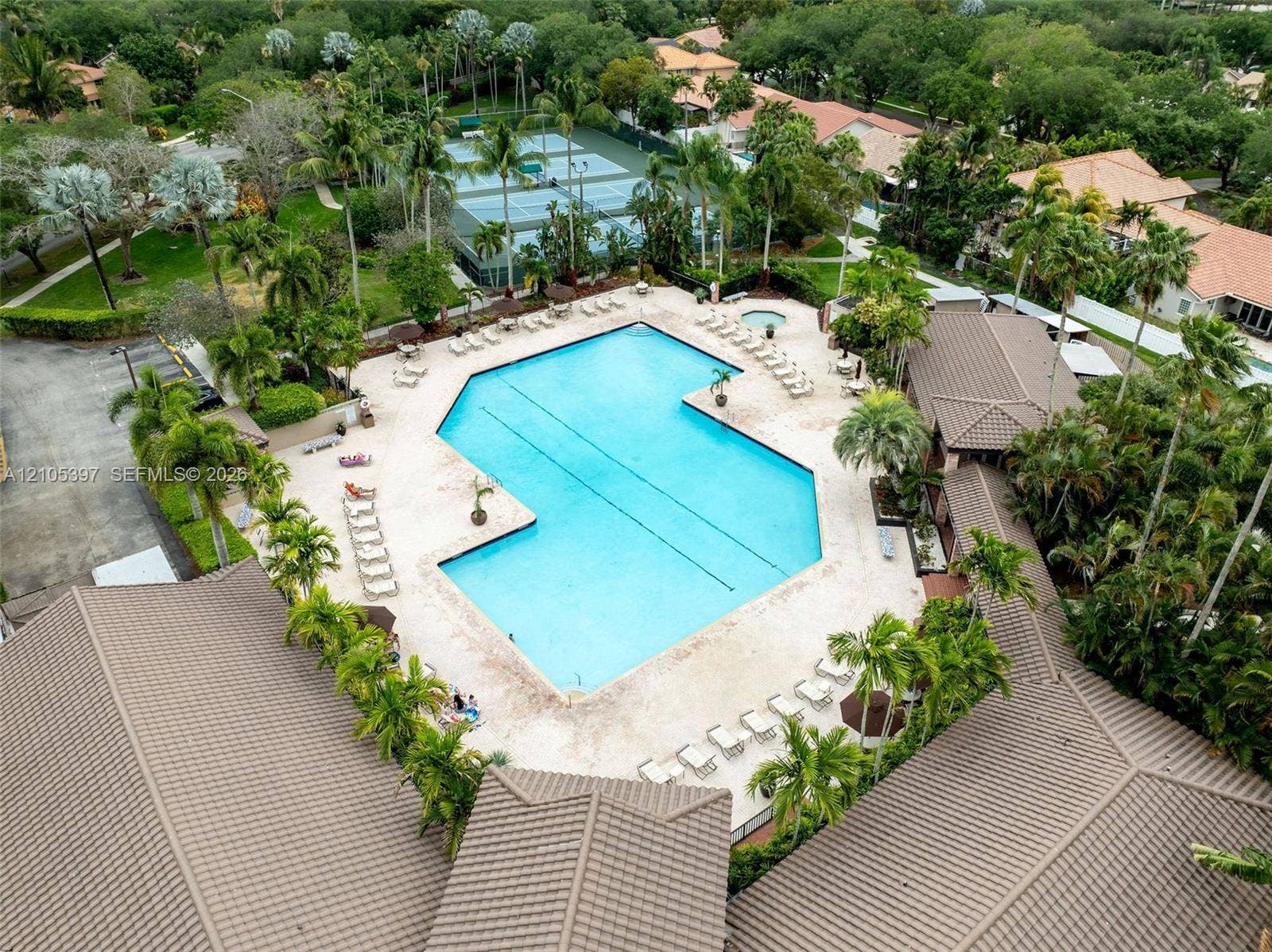 Large swimming pool with integrated spa, stone-paver pool deck, and tennis courts surrounded by mature palm trees and lush landscaping