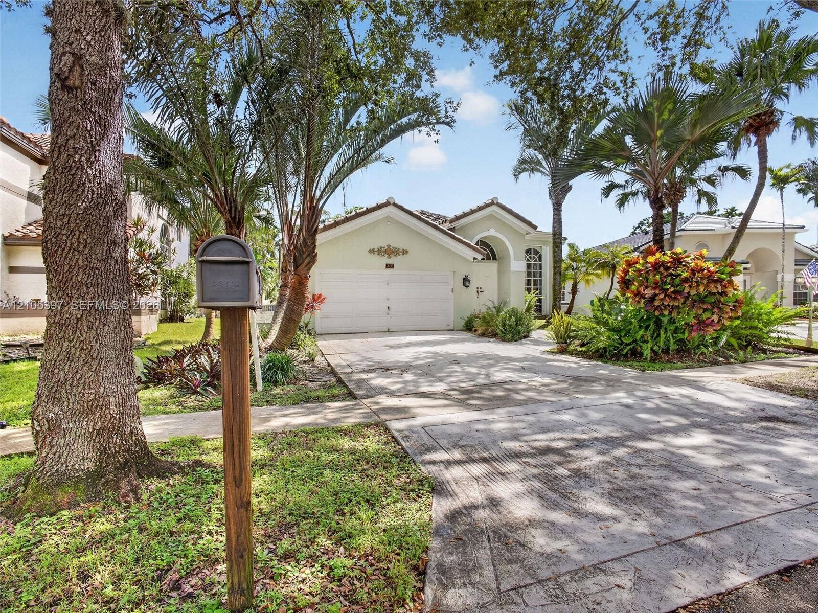 Exterior facade featuring a stucco finish, arched entryway, two-car garage, and mature landscaping