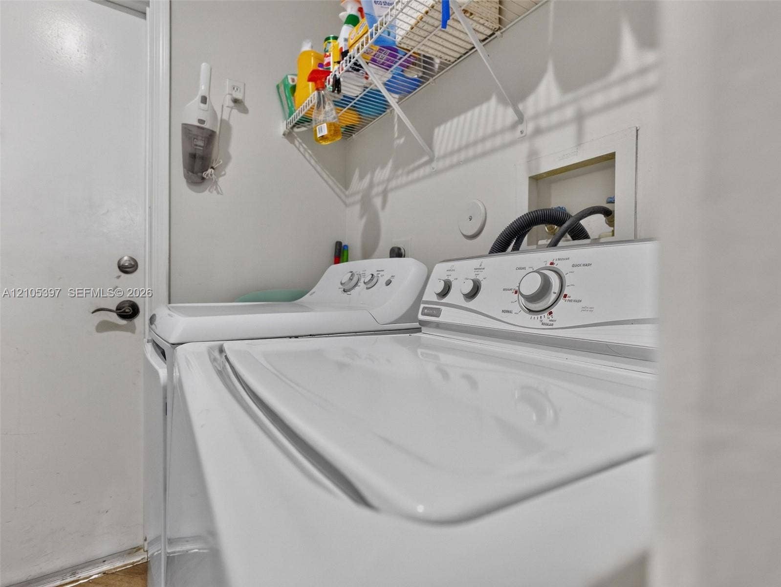 Dedicated laundry area featuring a white top-loading washer and dryer, integrated plumbing connections, and an overhead wire shelving unit