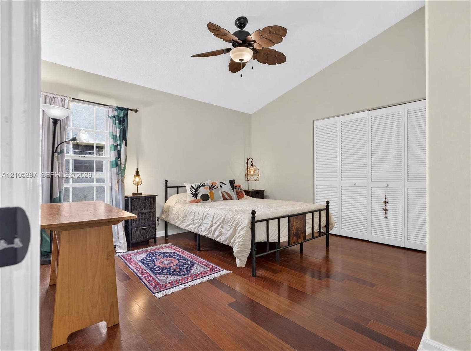 Vaulted ceiling featuring a leaf-style ceiling fan, wood-finish flooring, and white louvered bifold closet doors