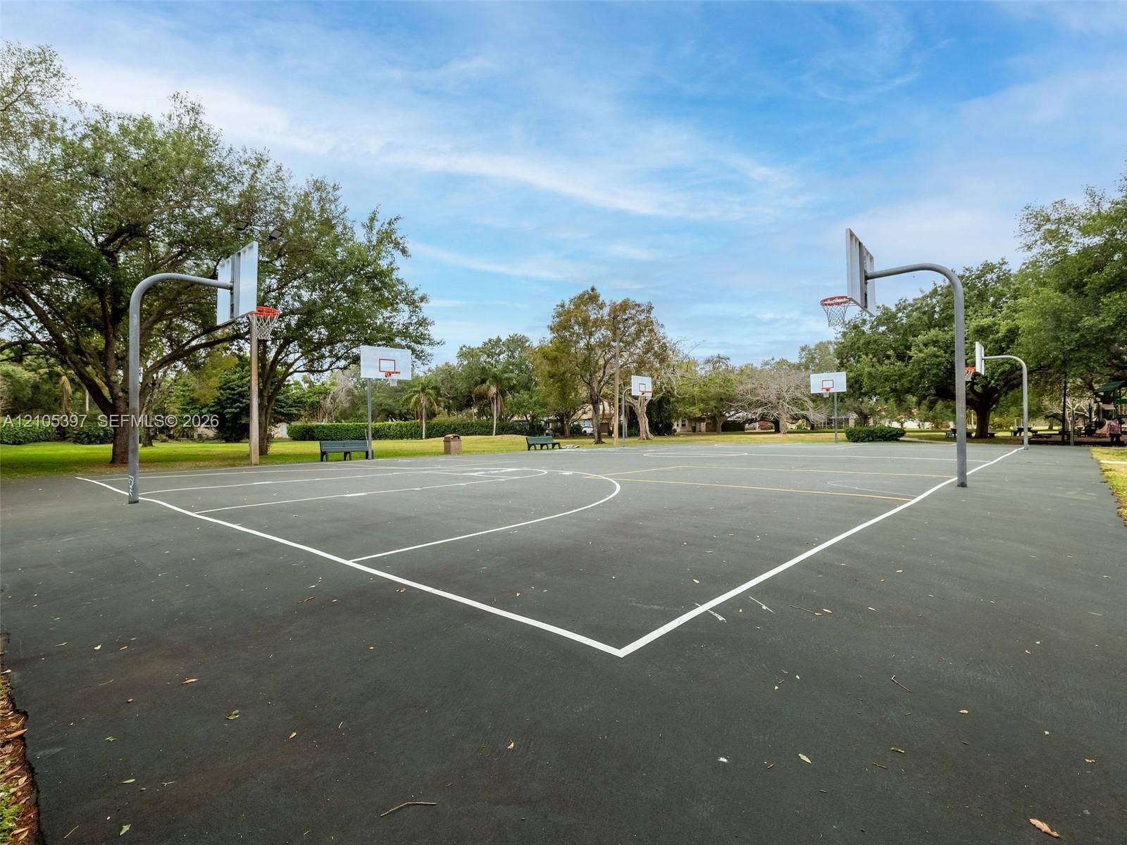 Outdoor sports court featuring paved surfacing, multiple basketball hoops, and perimeter park bench seating