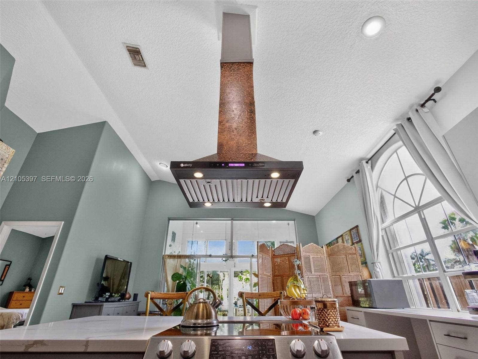 Custom hammered metal range hood, stone-surface island countertop, integrated stainless steel cooktop,