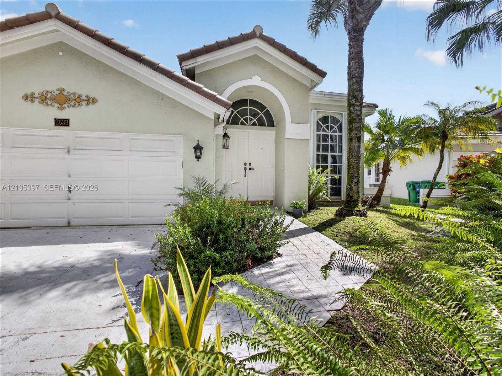 Stucco exterior featuring a 2022 tiled roof, double-entry front doors with an arched transom window, and a paved walkway
