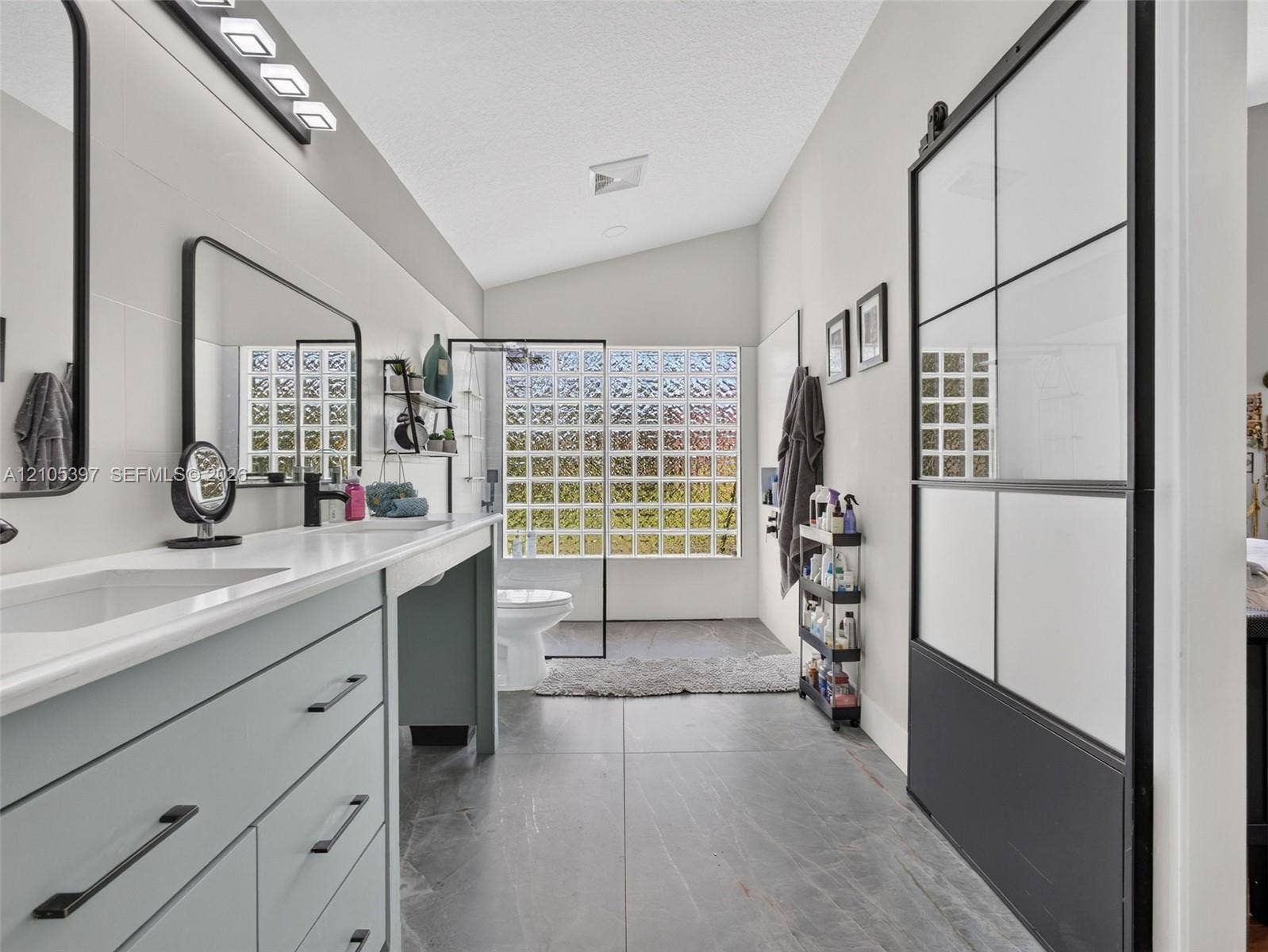 Bathroom featuring a dual-sink vanity with matte black hardware, large-format tile flooring, and a sliding door with a black grid frame