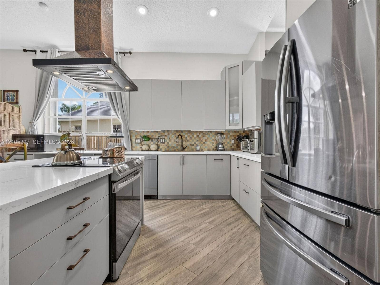 Kitchen featuring flat-panel cabinetry, quartz countertops, a copper-finish range hood, stainless steel appliances, and porcelain wood-finish flooring