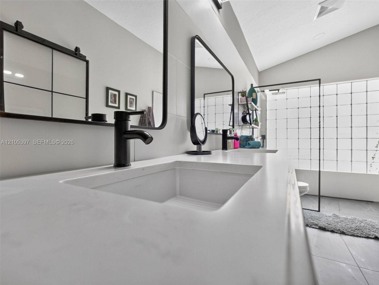 Dual-sink vanity featuring stone-finish countertops, matte black plumbing fixtures, framed mirrors, and large-format tile flooring