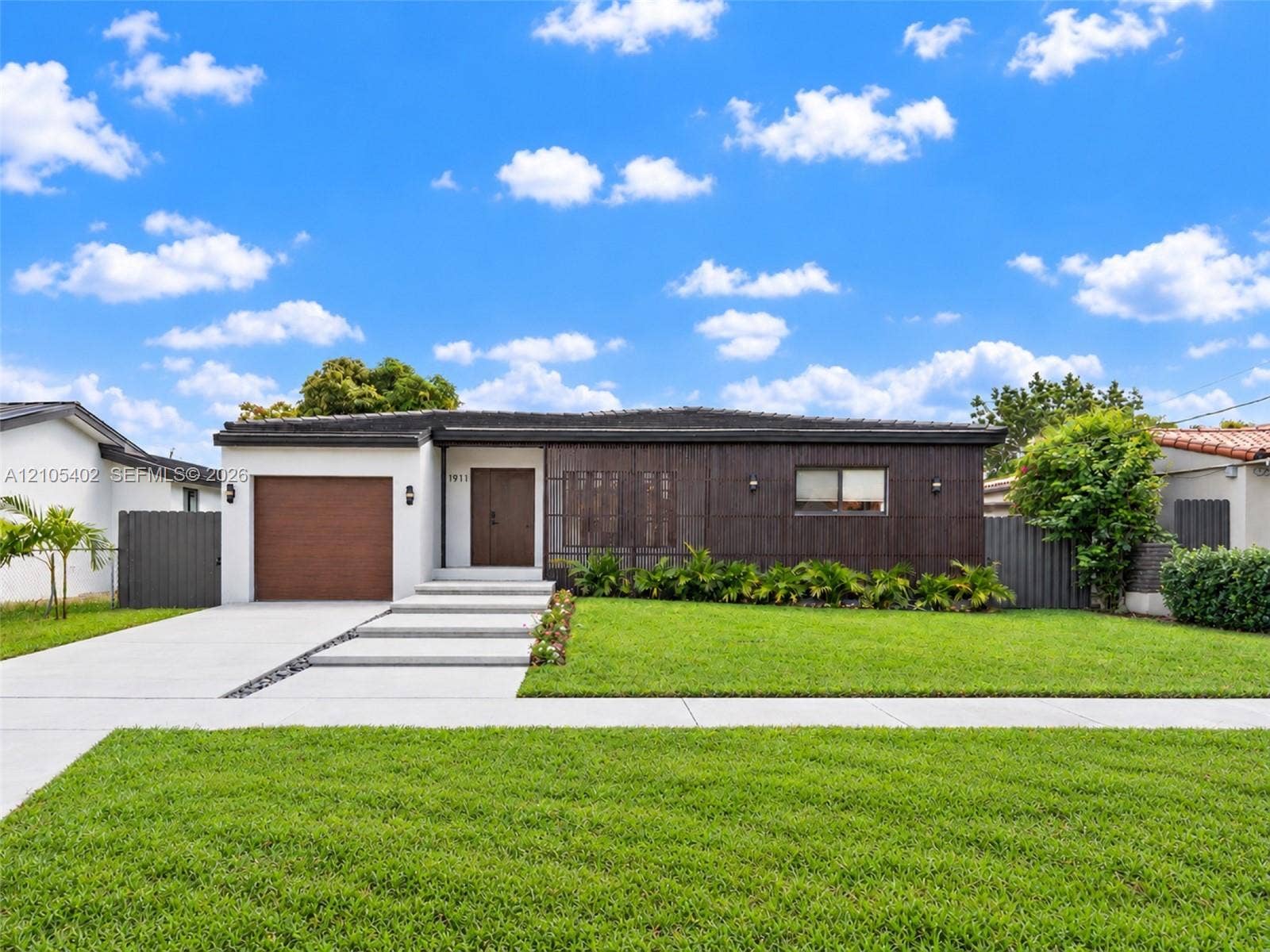 1911 SW 18th Avenue, Miami, FL 33145 Contemporary single-story exterior featuring dark wood-tone vertical siding, a concrete paver walkway, an integrated single-car garage, and a manicured front lawn