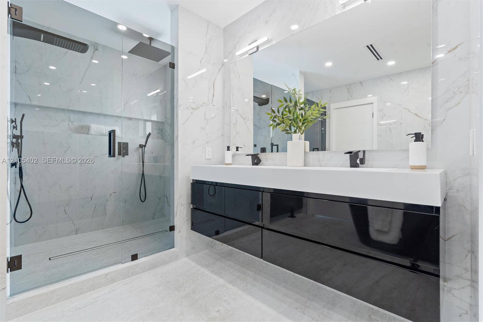 1911 SW 18th Avenue, Miami, FL 33145 Floating high-gloss black vanity featuring a dual-sink white countertop, wall-to-wall mirror, glass-enclosed walk-in shower with stone-finish wall tile, and matte black fixtures