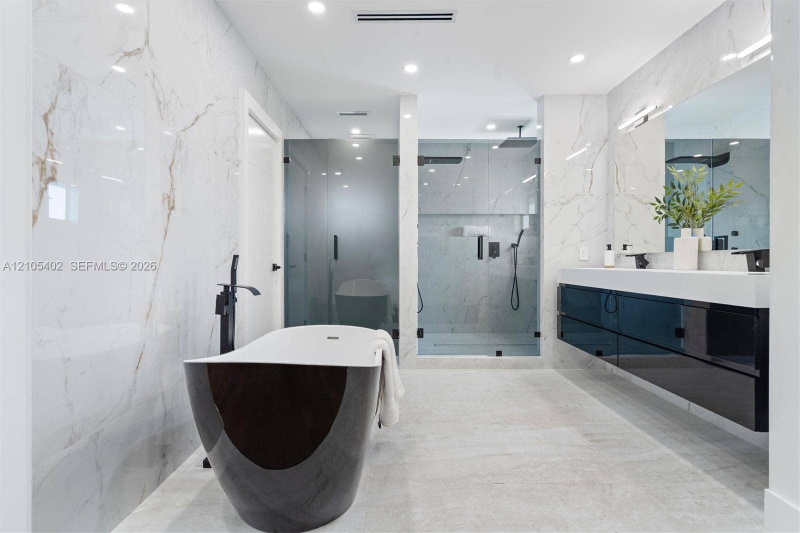 1911 SW 18th Avenue, Miami, FL 33145 Freestanding deep-soaking tub with floor-mounted matte black faucet, wall-to-wall stone-finish tile surround, wall-mounted floating dual vanity with integrated countertop, and walk-in glass-enclosed shower with matte black fixtures