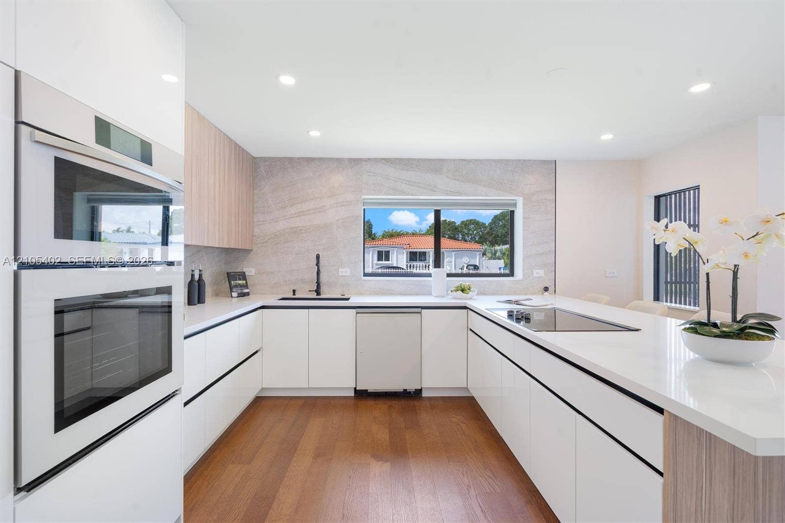 1911 SW 18th Avenue, Miami, FL 33145 Modern kitchen featuring white flat-panel cabinetry, wood-finish cabinetry accents, quartz countertops, a stone-patterned backsplash, and integrated stainless steel appliances