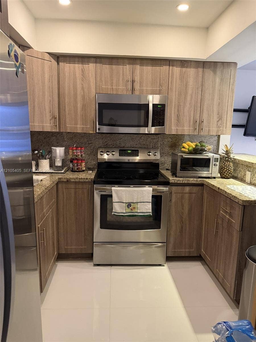 17570 Atlantic Boulevard, #119, Sunny Isles Beach, FL 33160 Stainless steel appliances, wood-finish cabinetry, recessed lighting, stone countertops, and a full-height stone-finish backsplash