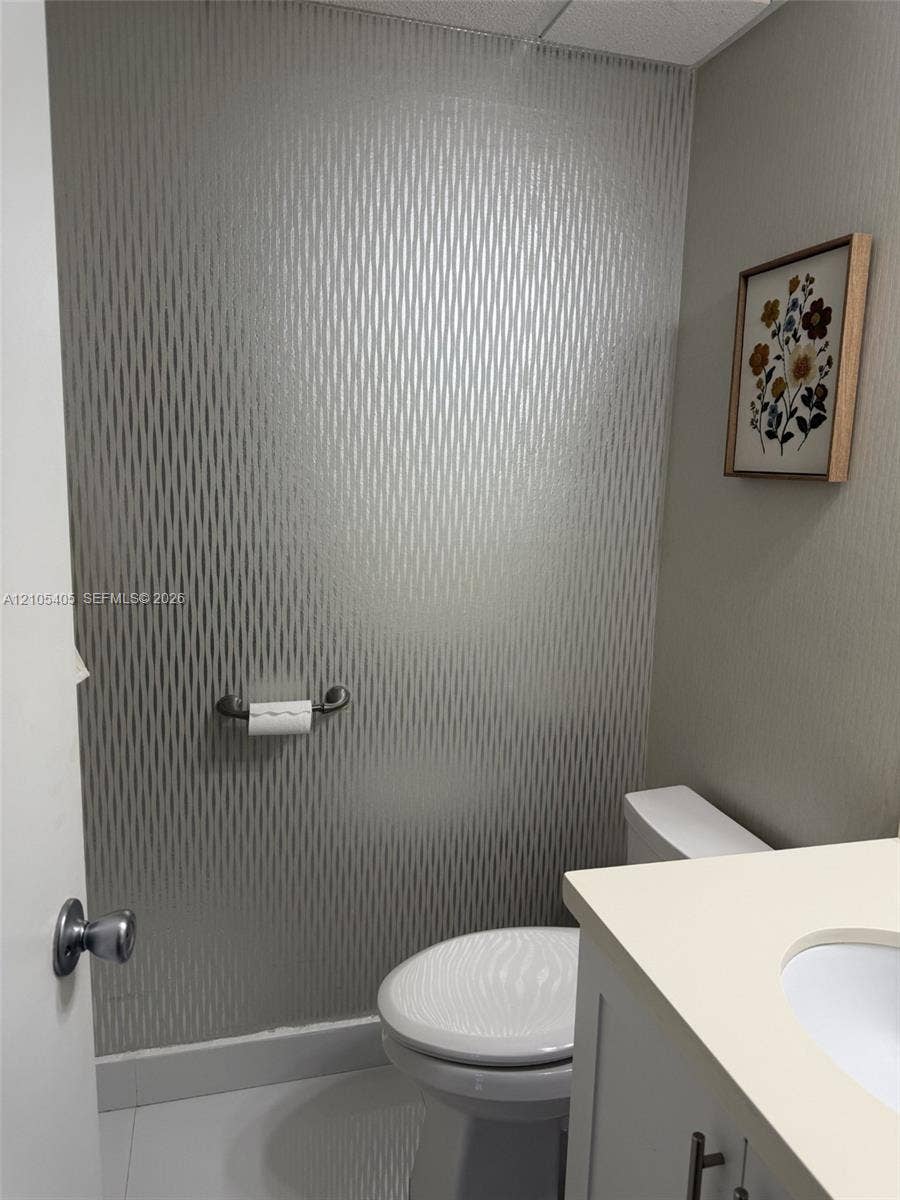 17570 Atlantic Boulevard, #119, Sunny Isles Beach, FL 33160 Powder room with patterned wall covering, white toilet, vanity with light-toned countertop, and integrated sink