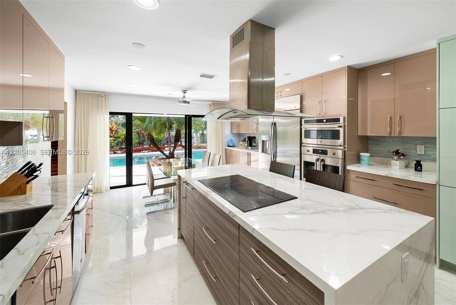 Gourmet kitchen featuring a large central island with integrated cooktop, stainless steel appliances, gloss-finish cabinetry, and a tile backsplash