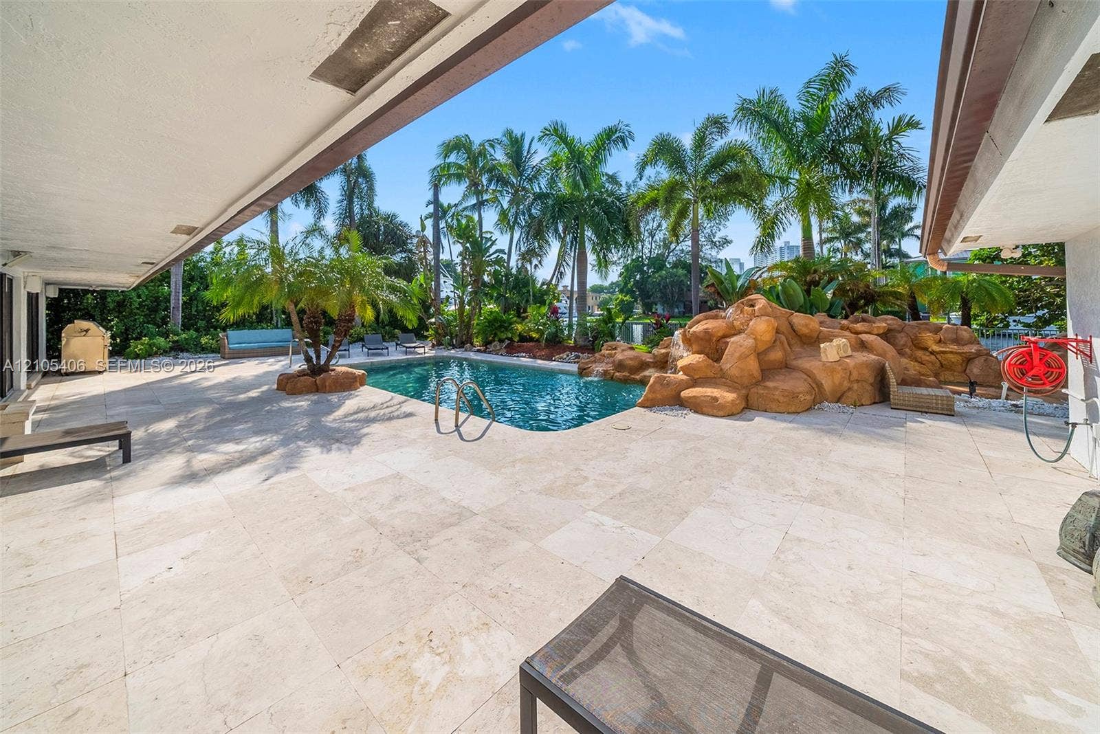 Expansive outdoor living area featuring a large swimming pool, rock water feature, and extensive patio paving