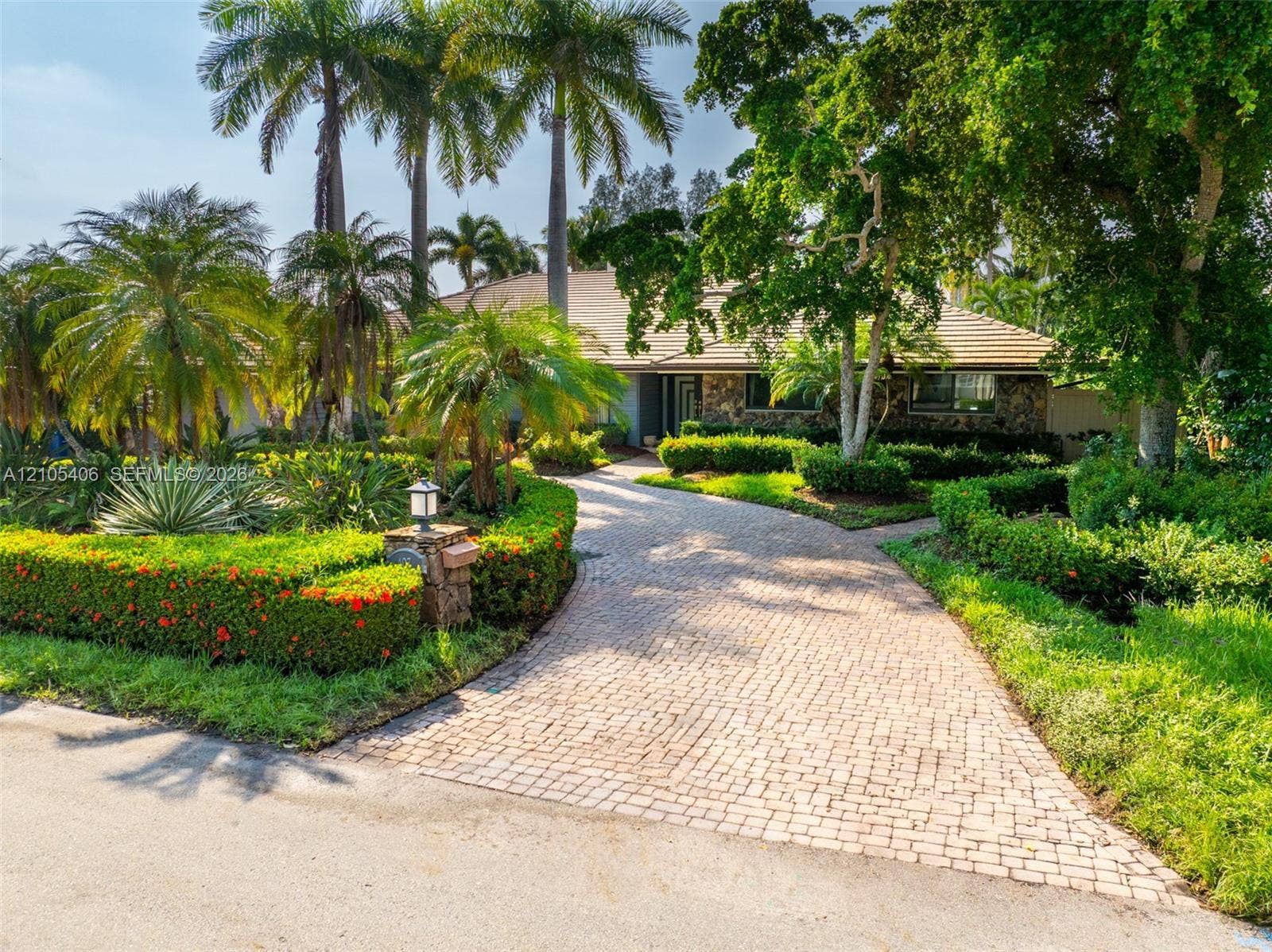 Paver driveway with a stone facade home, surrounded by mature landscaping and palm trees
