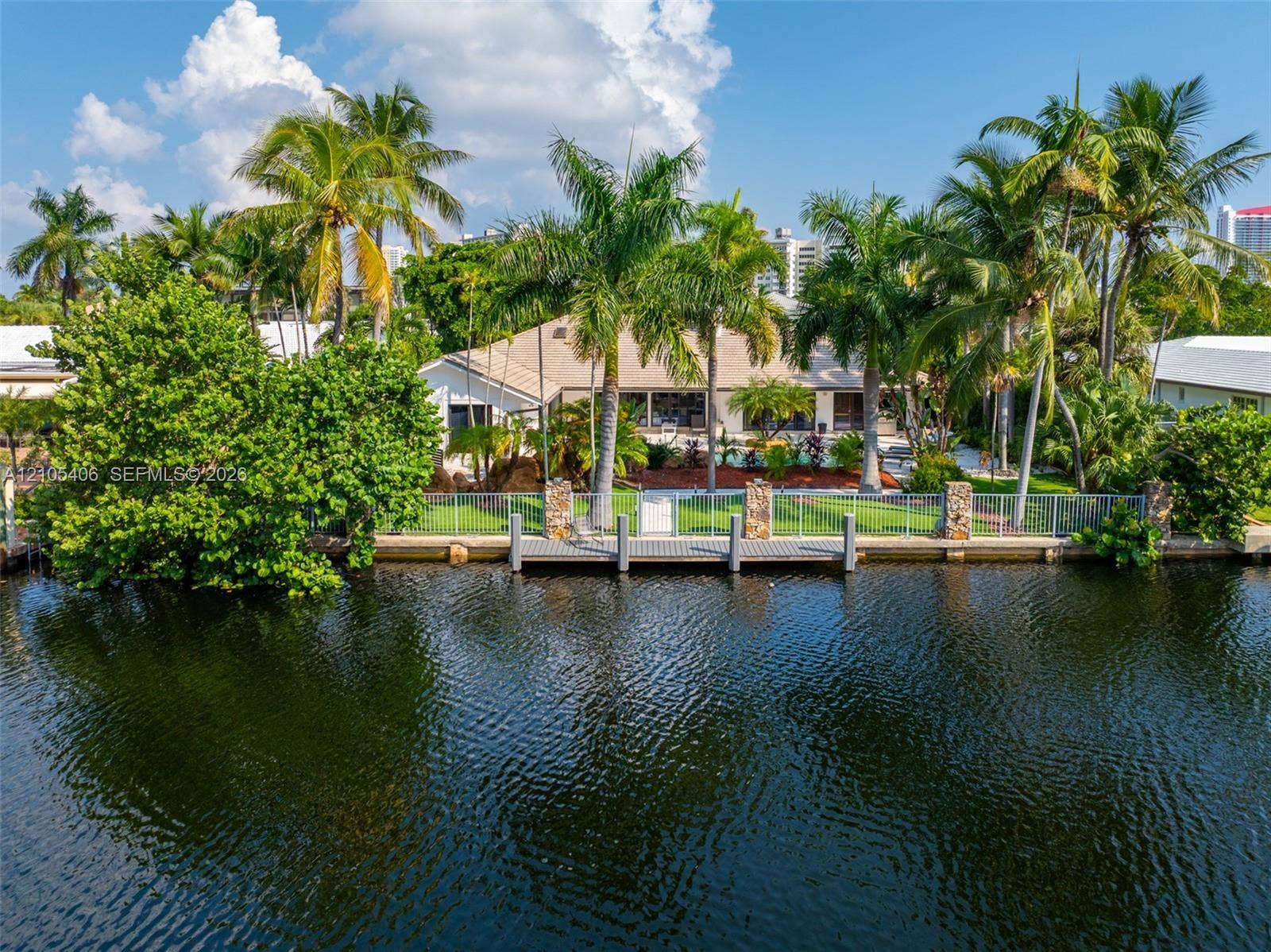 Waterfront property featuring a private dock with pilings, a manicured lawn, mature palm trees, and established landscaping