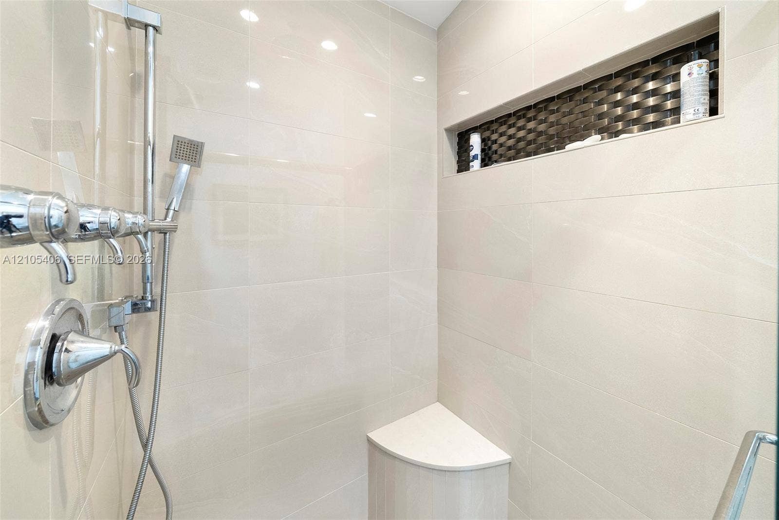 Shower with polished chrome fixtures, integrated niche with mosaic tile accent, a built-in corner bench, and large format wall tiling