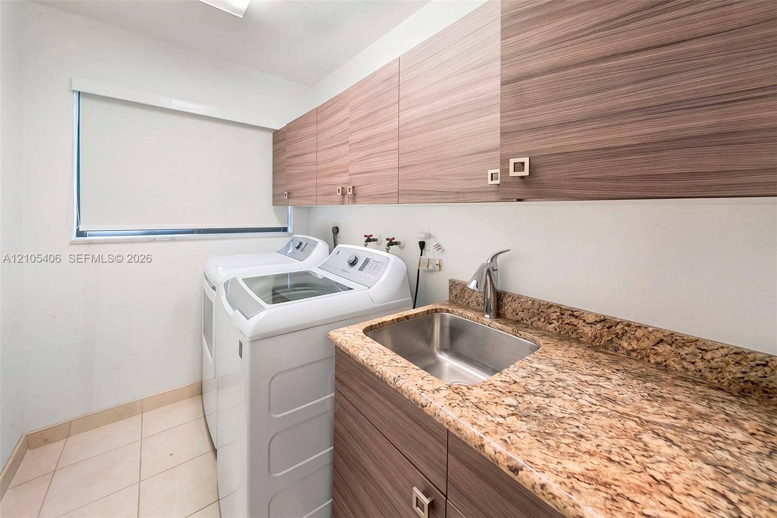 Laundry area featuring a utility sink, polished chrome faucet, stone-finish countertop, wood-finish cabinetry, and tiled flooring