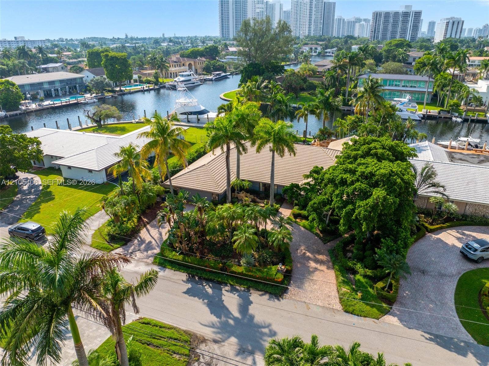 Waterfront property featuring a private dock, lush tropical landscaping, mature palm trees, a circular driveway, and a tiled roof
