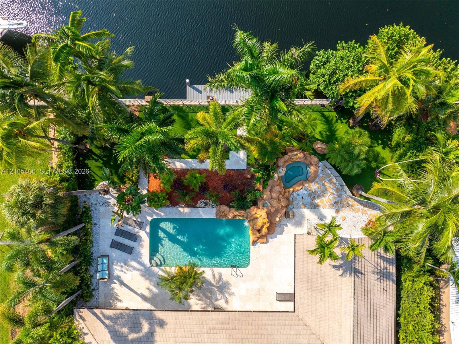 Waterfront property featuring a swimming pool, integrated spa, expansive paver patio, and lush tropical landscaping