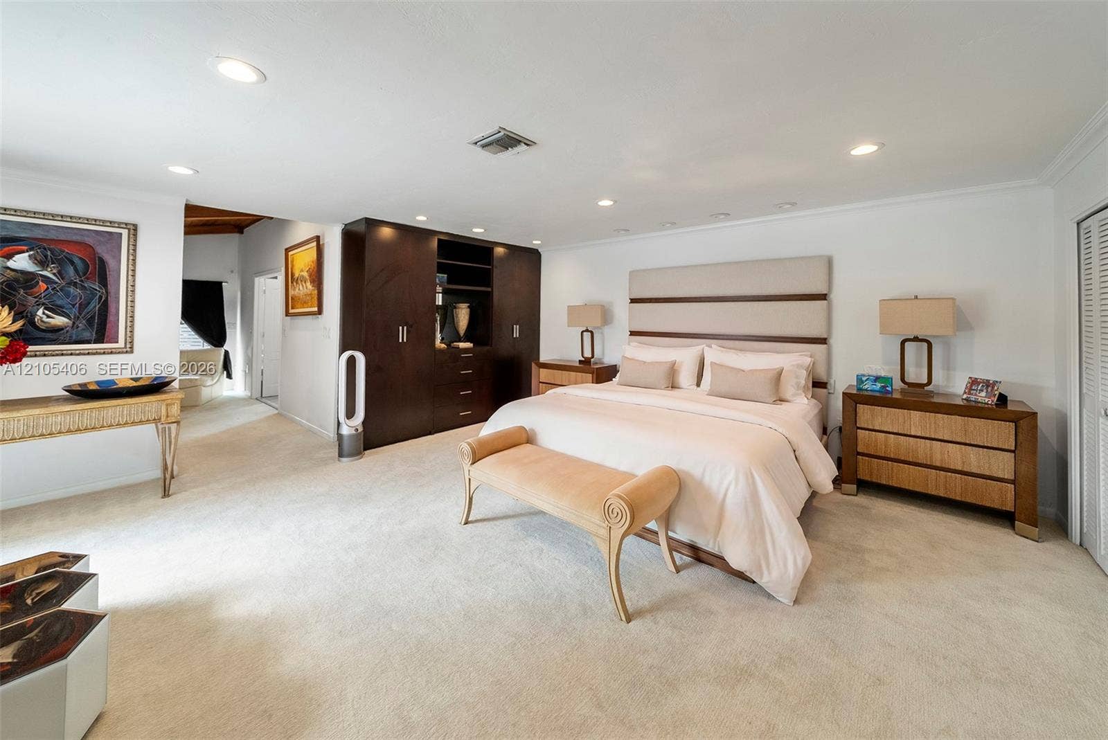 Recessed ceiling lighting, crown molding, built-in dark wood cabinetry, white shaker-style bifold closet doors, and light-colored carpeting
