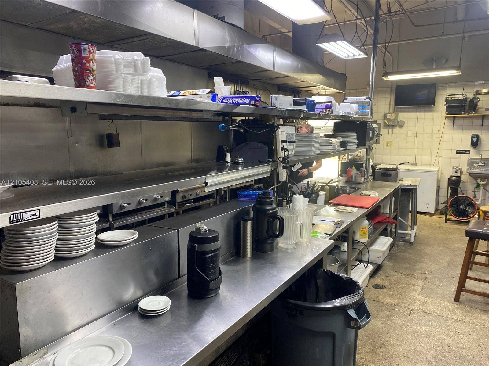 Commercial kitchen featuring stainless steel countertops, industrial shelving, a built-in griddle, and white tile walls