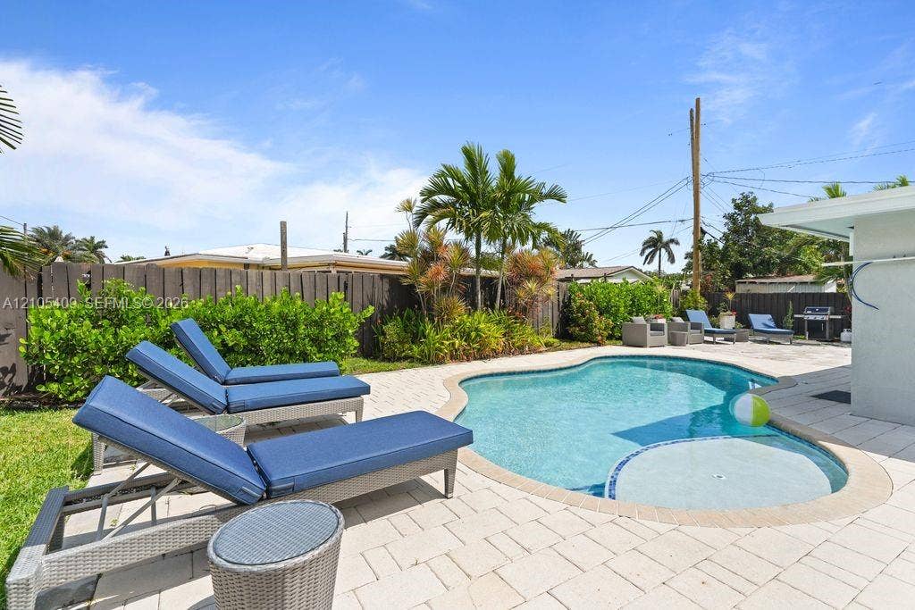 Freeform swimming pool with a spa, surrounded by paver decking, a wood privacy fence, and mature landscaping