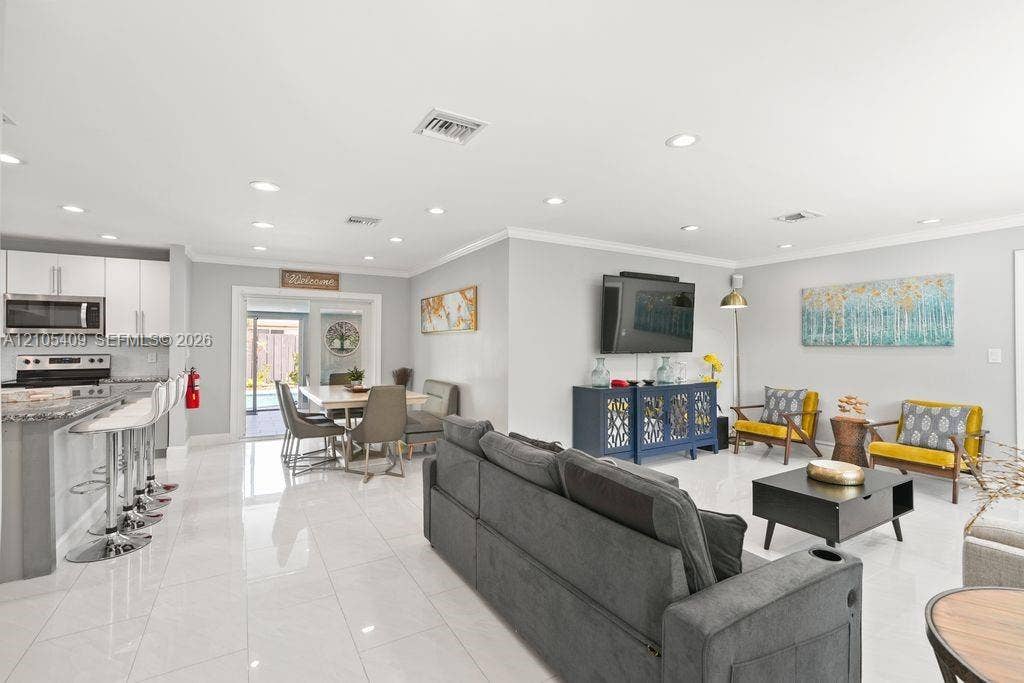 Recessed lighting, crown molding, white tile flooring, modern kitchen cabinetry with stainless steel appliances, and sliding glass doors to the exterior
